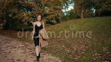 女人走过一个秋天的公园，冷的把棕色的外套放在身上保暖